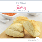 Drei eckige Scones auf hölzernem Brett mit kleinen weißen Schalen im Hintergrund, gefüllt mit mit oranger Marmelade und Butter.