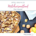 Apfel-Walnuss Milchreisauflauf in gläserner Backform auf einem Servierbrett auf schwarzem Untergrund. Eckige Teller, Äpfel und Walnüsse gegenüber platziert.