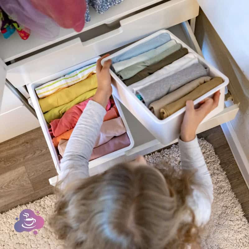 Kind, ordentliches Kinderzimmer beim Aufräumen und Kleidung sortieren für mehr Unabhängigkeit.